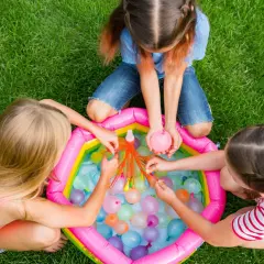 Bambine giocano con palloncini d'acqua in una piscina gonfiabile, perfetti giochi per feste di compleanno 7-8 anni.