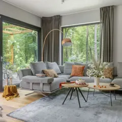 Nowoczesny salon z szarą sofą, stolikami kawowymi i widokiem na las. Inspiracja, jak urządzić salon nowocześnie.