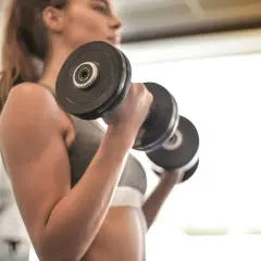 Mujer realizando ejercicios para fortalecer los brazos con pesas en un gimnasio.