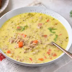Gęsta zupa z pora z serkiem topionym i mięsem mielonym, ozdobiona koperkiem. Obok kromki chleba.