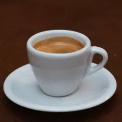 Ein weißer Becher mit cremigem, doppeltem Espresso steht auf einer Untertasse.