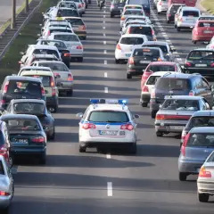 Kork na drodze, gdzie pojazd uprzywilejowany z włączonymi sygnałami świetlnymi próbuje się przebić przez sznur samochodów.