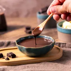 Flüssige Schokosauce tropft von einem Holzlöffel in eine Schale. Die Sauce wird hart, wenn sie abkühlt.
