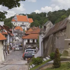 Ulica w Kazimierzu Dolnym z widokiem na kościół i wzgórza. Widać kamienne domy, brukowaną drogę i turystów. Kazimierz Dolny atrakcje zachwycają.
