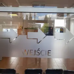 Szklane drzwi z matowymi strzałkami i napisem "WEJŚCIE".