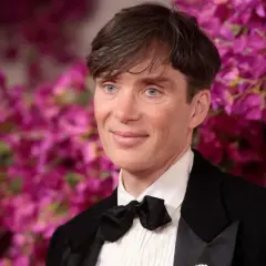 Cillian Murphy, l'attore di Oppenheimer, con un sorriso enigmatico e occhi azzurri penetranti, indossa un elegante smoking con papillon nero.