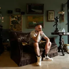 Uomo pensieroso su divano di velluto, circondato da quadri e oggetti d'antiquariato. Forse sta pensando a testi sch cartine Cartier.