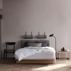 Ein minimalistisches schlafzimmer skandinavisch mit einem Holzbett, grauen Kissen und einer Stehlampe. Zwei gerollte Decken hängen an der Wand.