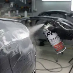 Un guante negro rocía imprimación en un coche. Es importante lijar la imprimación antes de pintar para un acabado perfecto.