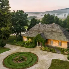 Drewniany dom z zielenią, okrągły klomb z kwiatami i mgliste wzgórza w tle. Idealne miejsce na odkrywanie ciekawych atrakcji.