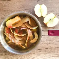 Gotuje się kompot z obierek jabłek, obok leżą połówki jabłek.