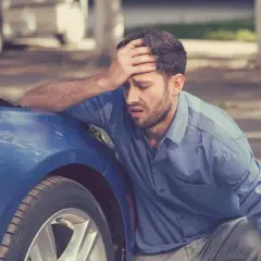 Hombre frustrado con el capó abierto de su coche azul. A veces, merece la pena arreglar un coche de 20 años.