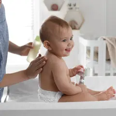 Mama delikatnie wmasowuje w plecy dziecka olejek migdałowy do kąpieli. Uśmiechnięty maluch trzyma buteleczkę z płynem.