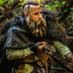 En skäggig krigare med pilbåge i en skog, redo för strid som den sista häxjägaren.