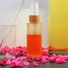 Zutaten für anti aging creme selber machen: ein Becherglas mit Pipette, eine Sprühflasche mit orangefarbener Flüssigkeit und ein großes Glas mit gelbem Öl.