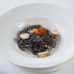 Pasta negra con trozos de pescado, huevas de salmón y yema de huevo. La tinta de calamar, ingrediente principal, aporta un sabor único y propiedades beneficiosas.