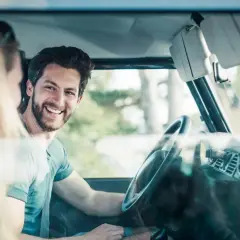 Uśmiechnięty mężczyzna za kierownicą samochodu, obok pasażerka.
