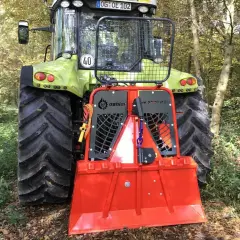 Ein grüner Traktor mit einer roten Forstseilwinde im Wald. Die Seilwinde ist bereit für den Einsatz, um Holz zu ziehen.