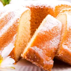 Puszysta babka wielkanocna, oprószona cukrem pudrem, z kawałkami ciasta i kwiatową dekoracją.