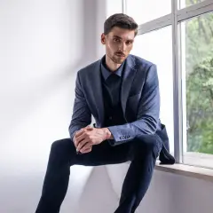 Elegancki mężczyzna w granatowej koszuli i marynarce, zastanawia się, jakie spodnie do niebieskiej koszuli będą najlepszym wyborem.
