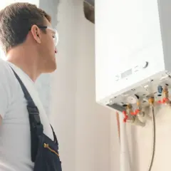 Technik w okularach ochronnych sprawdza instalację gazową. Wykonuje odpowietrzanie pieca gazowego, dbając o jego prawidłowe działanie.