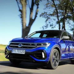 Niebieski Volkswagen T-Roc R pędzi po wiejskiej drodze, otoczony drzewami i polami.