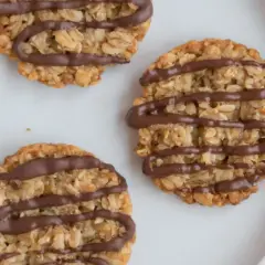 Nyttiga havrekakor utan socker, dekorerade med choklad, ligger på en vit tallrik bredvid guldfärgade skedar.