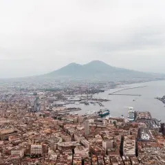 Panoramic view of Napoli, Naples, with Mount Vesuvius looming in the distance over the bustling port and city.