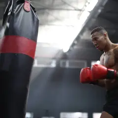 A boxer training intensely, sweat glistening on his skin as he throws punches at a heavy bag in a dimly lit gym.