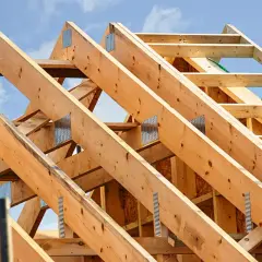 Structure en bois d'une charpente simple, avec des poutres assemblées par des équerres métalliques sous un ciel bleu.