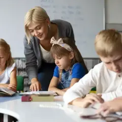 Nauczycielka pomaga uczniom w lekcji przy biurku w klasie.