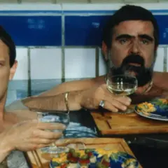 Dwóch mężczyzn w wannie, jeden z wąsami, pije wino i je przekąski. Scena z filmu "Kiler", rok produkcji 1997.