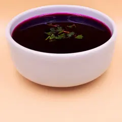 Aromatic barszcz czerwony domowy, głęboki kolor buraków, ozdobiony świeżymi ziołami, w białej miseczce.
