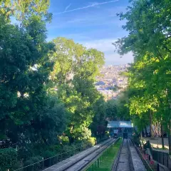 Vue sur le funiculaire de Montmartre, avec Paris en arrière-plan. Les arbres verdoyants encadrent la scène.