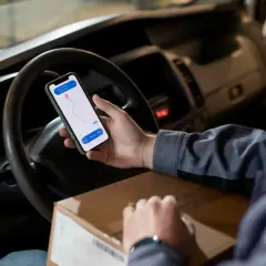Kierowca sprawdza trasę na telefonie, trzymając paczkę. Aplikacja nawigacyjna pokazuje punkty odbioru i dostawy, ułatwiając pracę w **srs dpd**.