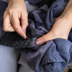 Ręce zszywają ciemną łatkę na rozerwanej kurtce puchowej. Dowiedz się, jak naprawić rozerwaną kurtkę puchową.