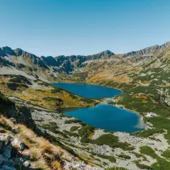 Widok na szlak z Morskiego Oka do Doliny Pięciu Stawów. Dwa turkusowe jeziora otoczone skalistymi szczytami i zieloną roślinnością.