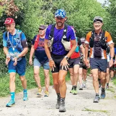 Coureurs en tenue de trail, certains avec des sacs d'hydratation, sur un sentier boisé. Le coureur au centre, portant une casquette bleue, semble en pleine course, peut-être en quête d'un record gr34.