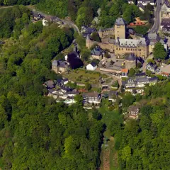 Luftaufnahme eines Schlosses, eingebettet in grüne Wälder. Die Burg ist ein beliebter Ort für Veranstaltungen und Ausflüge.