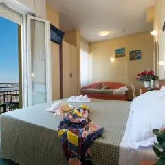 Pokój hotelowy z widokiem na morze, idealny na loty do Rimini. Na łóżku leży słomkowy kapelusz i kolorowy szal.