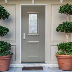 Une porte d'entrée grise avec une fenêtre décorative, encadrée par deux grands pots de plantes taillées. Idéal pour savoir comment changer une porte d'entrée.