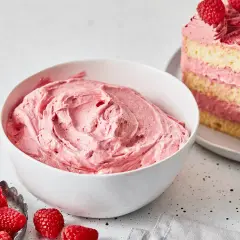 Schüssel mit cremiger Buttercreme mit Pudding und Himbeeren. Daneben ein Stück Kuchen mit derselben Füllung.