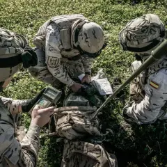Soldados del ejército español con uniforme multicam revisan equipo en el campo.