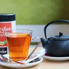 Szklanka z bursztynowym naparem, obok czajniczek i puszka z napisem "Rooibos con Flor". Czas na chwilę relaksu z rooibos.
