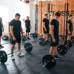 Mężczyźni w czarnych strojach ćwiczą z ciężarami w sali treningowej. Czy crossfit jest zdrowy? Ta grupa wydaje się to sprawdzać.