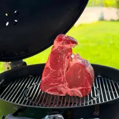 Una succulenta bistecca alla fiorentina cruda riposa sulla griglia di un barbecue, pronta per essere cucinata all'aperto.