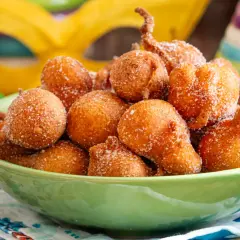 Frittelle di una volta, dolcetti dorati cosparsi di zucchero, pronti per il Carnevale. Maschere e coriandoli sullo sfondo.