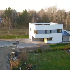 Nowoczesny dom w trakcie prac wykończeniowych, obok koparka i materiały budowlane. To projekt zamienny po zakończeniu budowy.