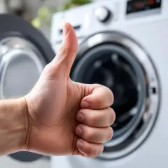 Pouce levé devant une machine à laver ouverte, signe d'un branchement machine à laver réussi.