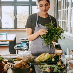 Frau bereitet frisches Gemüse für eine gesunde Ernährung zu. Kräuter, Mais und Pilze auf dem Tisch, inspiriert von der planetary health diet.